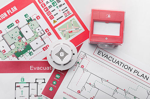 Plans d'évacuation, détecteur de fumée et point d'appel manuel sur fond blanc